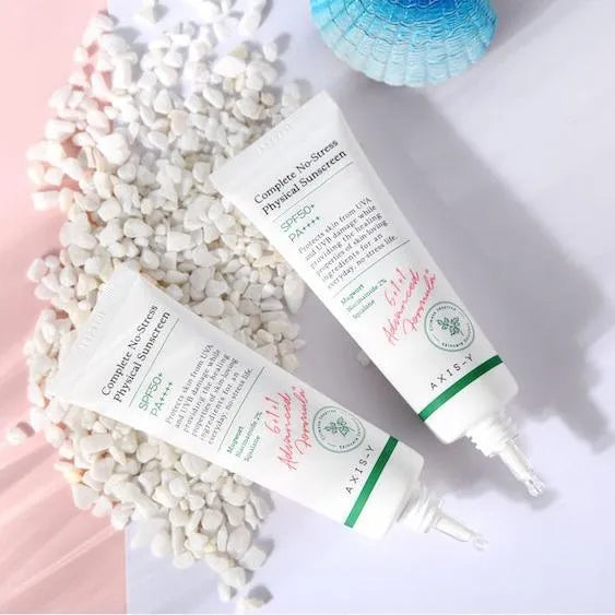 Axis-Y Complete No-Stress Physical Sunscreen tubes on white pebbles, Korean skincare product