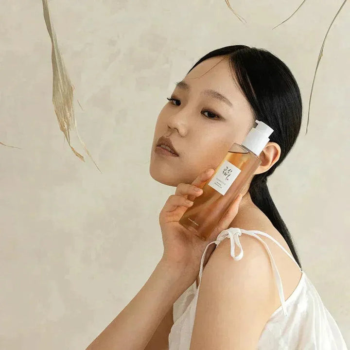 Woman holding Beauty of Joseon Ginseng Cleansing Oil, Korean skincare product, neutral background