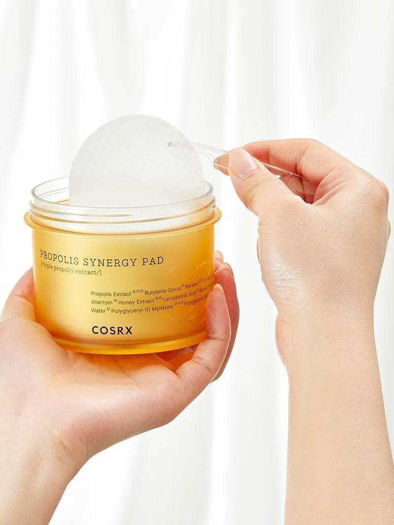 Hand holding COSRX Propolis Synergy Pad, a Korean skincare product, against a white background.