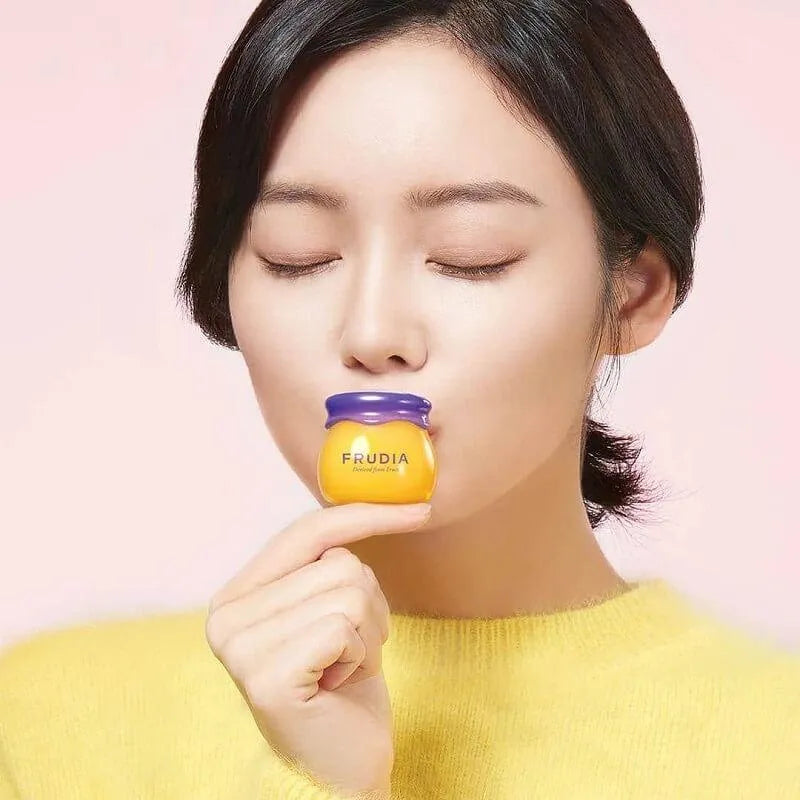 Woman with closed eyes holding Frudia Blueberry Hydrating Honey Lip Balm, Korean skincare product
