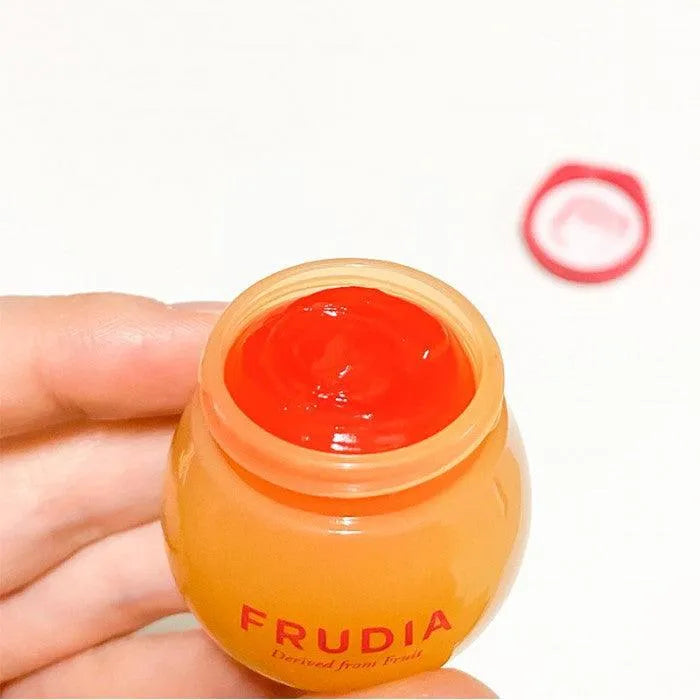 Hand holding Frudia Pomegranate Honey 3-in-1 lip balm jar, Korean skincare product
