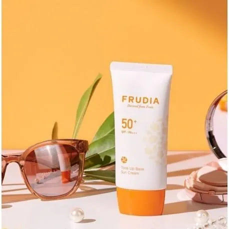 Frudia Tone Up Base Sun Cream SPF50 on table with sunglasses, pearl, and compact, Korean skincare