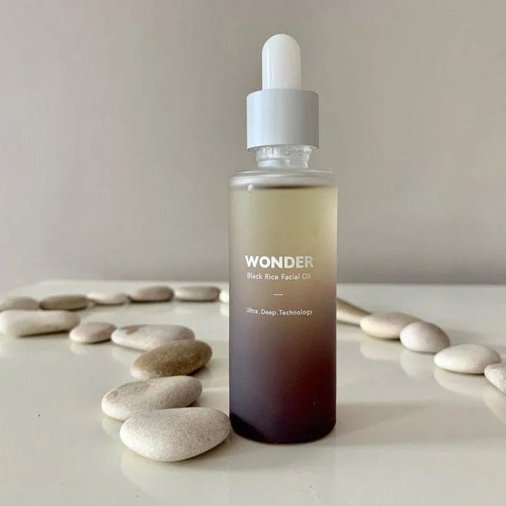 Haruharu Wonder Black Rice Facial Oil bottle on white table with smooth stones, Korean skincare