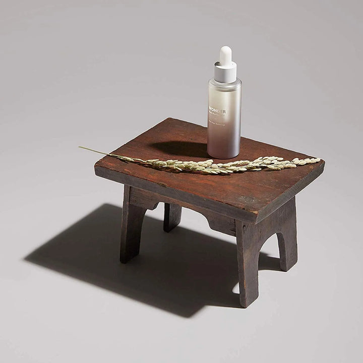 Haruharu Wonder Black Rice Facial Oil on wooden stool with rice stalk, Korean skincare product