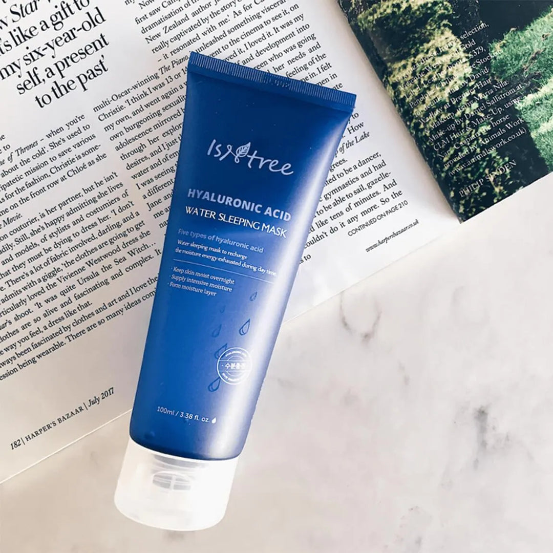 Isntree Hyaluronic Acid Water Sleeping Mask tube on marble next to an open magazine, Korean skincare