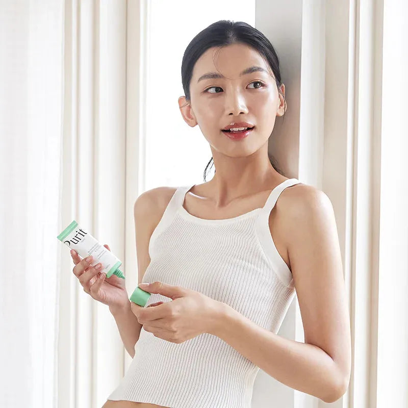 Young woman applying Purito Korean skincare cream by a bright window, Me Time Groningen