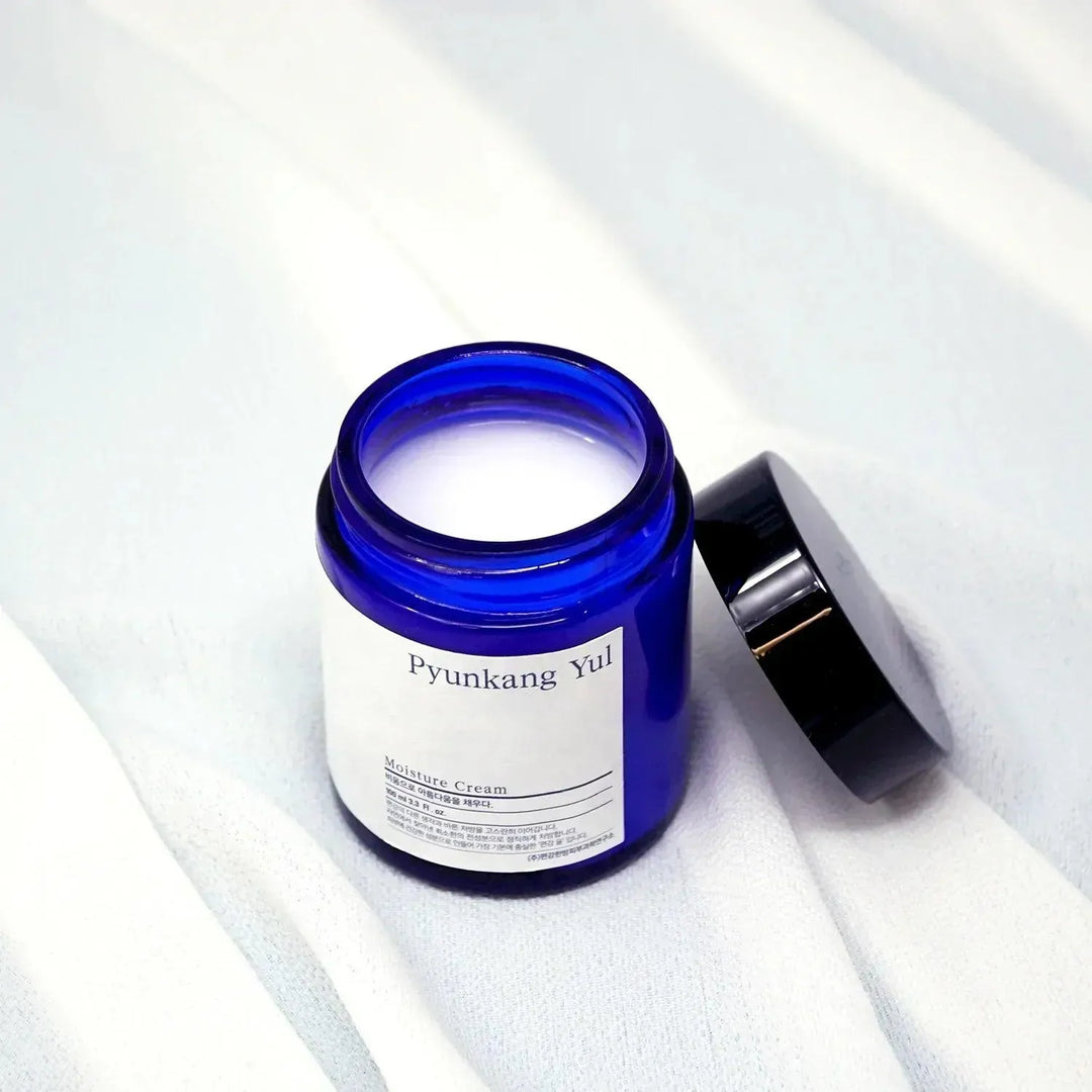 Pyunkang Yul Moisture Cream in blue jar on soft white fabric, Korean skincare Nederland